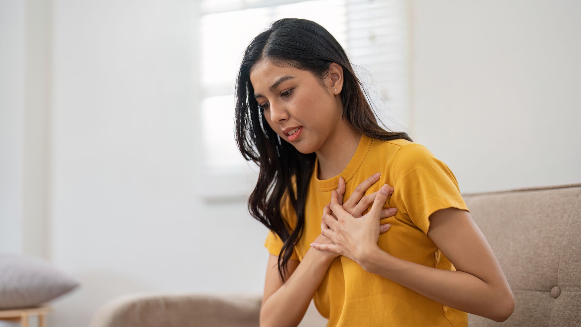 A young woman clutching her chest in discomfort, illustrating how anxiety can cause chest pain and related symptoms.