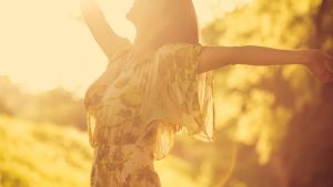 A woman standing in sunlight with open arms, symbolizing freedom, self-acceptance, and the celebration of neurodiversity.