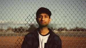 A young boy standing in front of a chain-link fence, symbolizing the genetic and environmental factors influencing autism prevalence in boys.