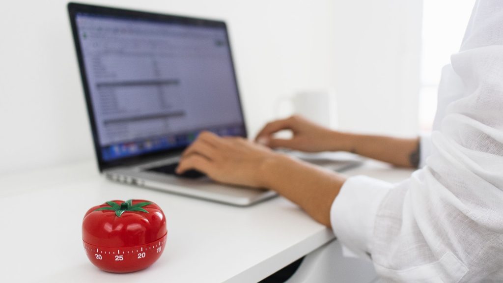 Person working on a laptop with a red tomato timer nearby, illustrating the 20 Minute Rule for ADHD and time management focus.