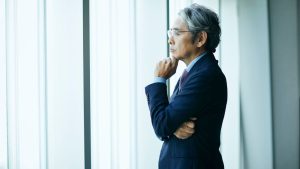 Older adult looking out a window in deep thought, illustrating the question ‘Can I be autistic and not know it?