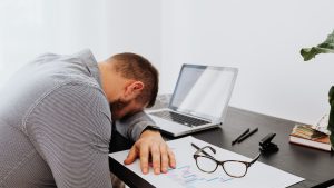 Person with head resting on desk beside a laptop, symbolizing fatigue and overwhelm associated with how to tell if you’re in autistic burnout.