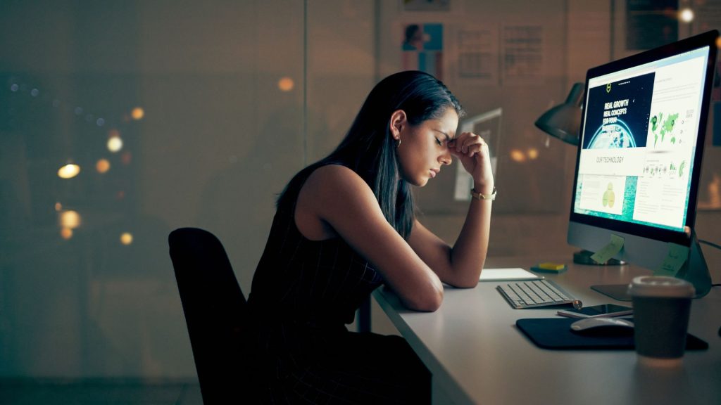 Person sitting at a desk late at night, appearing exhausted and overwhelmed, representing what does AuDHD burnout feel like.